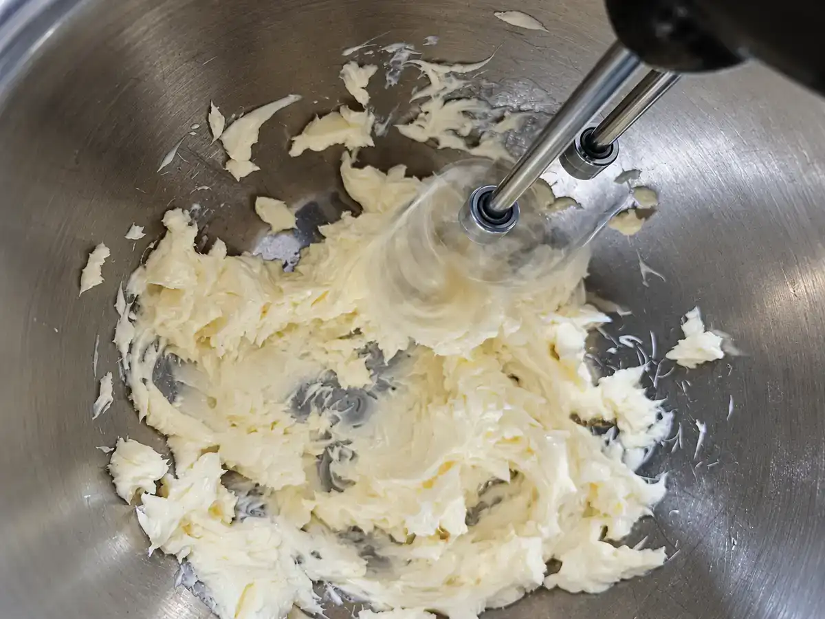 Softened butter being beaten with a hand mixer in a stainless-steel bowl