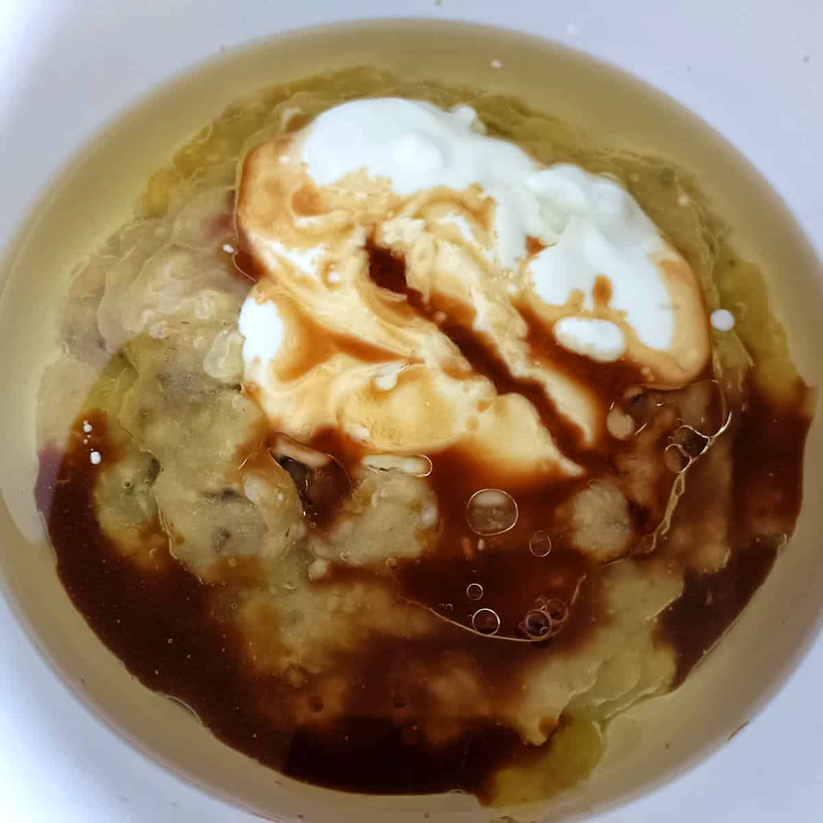 Mashed banana mixed with yogurt, butter, and vanilla for eggless strawberry banana muffins