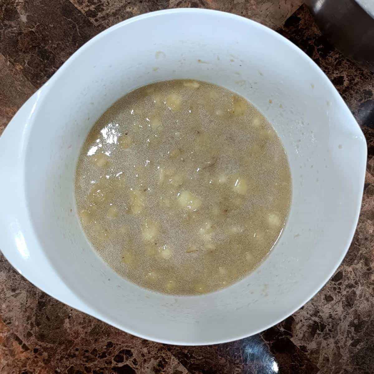 Whisked wet ingredients with mashed banana in a white bowl for vegan banana pecan muffin batter