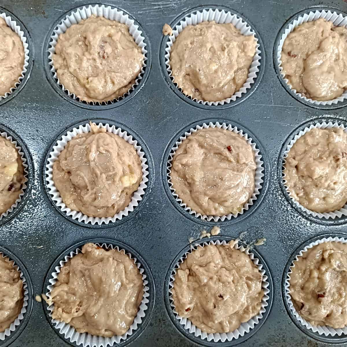 Vegan banana pecan muffin batter divided into paper-lined muffin cups in a baking pan