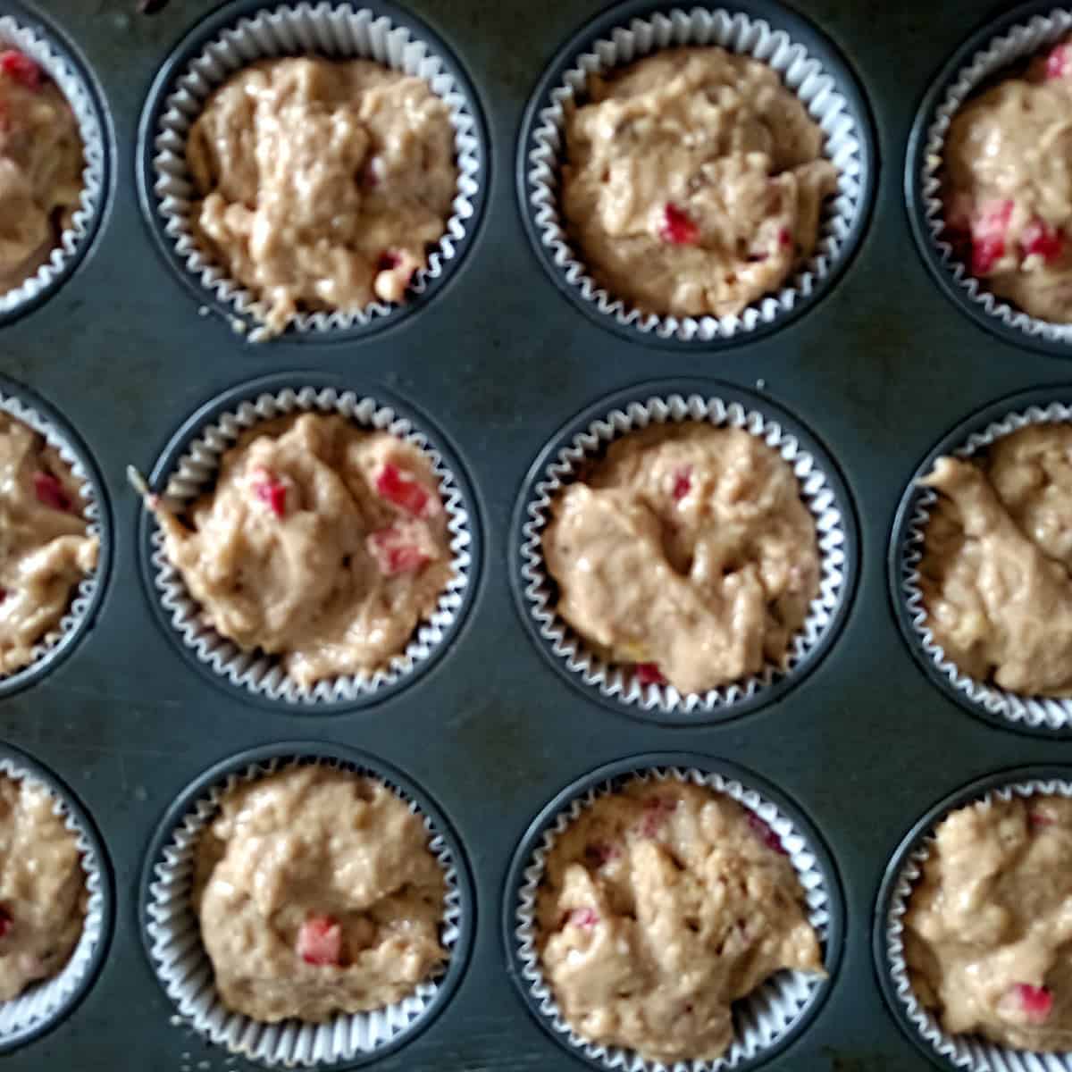 Muffin cups filled with strawberry banana muffin batter