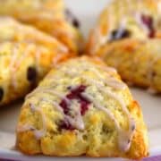 A close-up of golden, flaky eggless blueberry scones drizzled with a sweet glaze. The scones have a crisp exterior with bursts of juicy blueberries inside.
