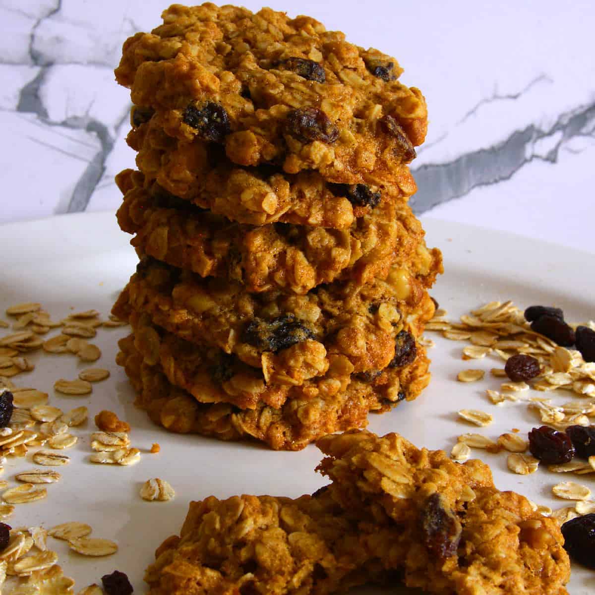 A tall stack of golden vegan oatmeal raisin cookies with visible oats and plump raisins, showing a thick, chewy texture.