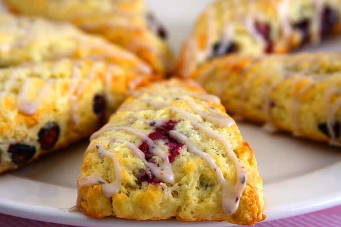 Close-up of freshly baked eggless blueberry scones with a golden crust, drizzled with a sweet glaze. The juicy blueberries peek through the flaky texture.