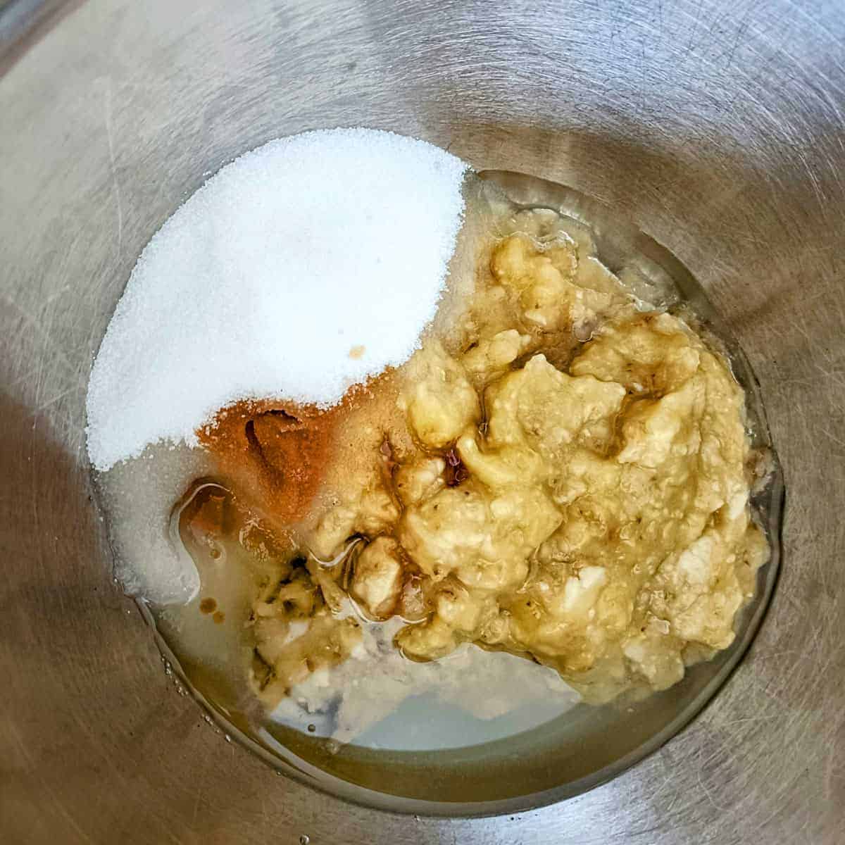Mashed bananas, sugar, oil, and vanilla in a bowl before mixing for eggless banana muffins