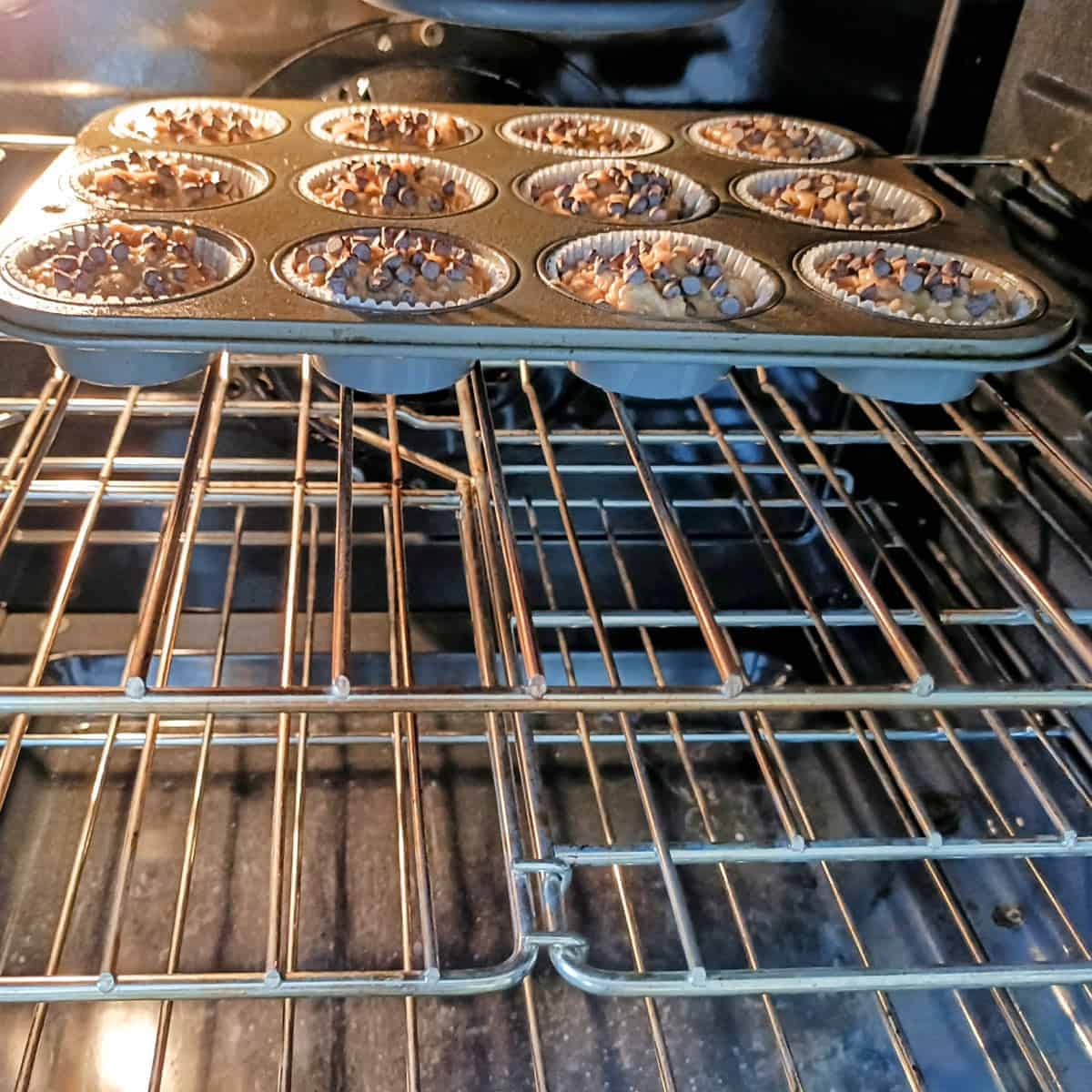 Muffin tray placed in oven baking banana chocolate chip muffins