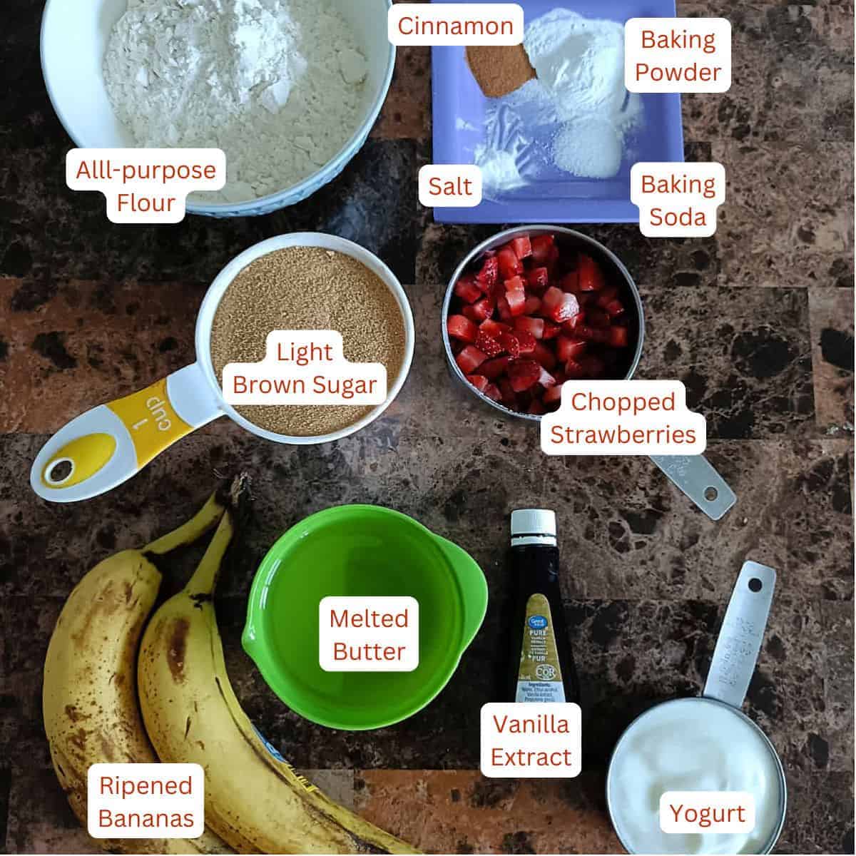 Ingredients for strawberry banana muffins including bananas, fresh strawberries, yogurt, flour, sugar, butter, and vanilla extract